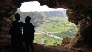 A photo from inside a scenic mountain cave in Puerto Rico, showing two people in silhouette in front of a grand tropical view