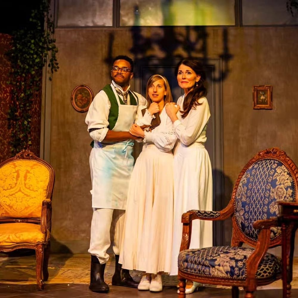 Beside ornate wooden armchairs, Buchanan, wearing a white apron, stands affectionately with the women, wearing white dresses