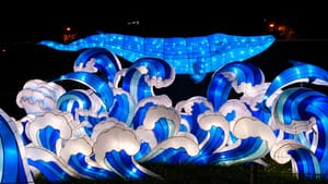 At night, lanterns shaped as ocean waves crash on the grass, a whale hovering over and behind the waves