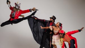 Three people in Nutcracker attire to the right look on to a fourth wearing a mouse head mask leaps in the air