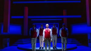 A scene from Choir Boy. Five young Black men in khakis and red vests face the audience, a spotlight on one in front, singing