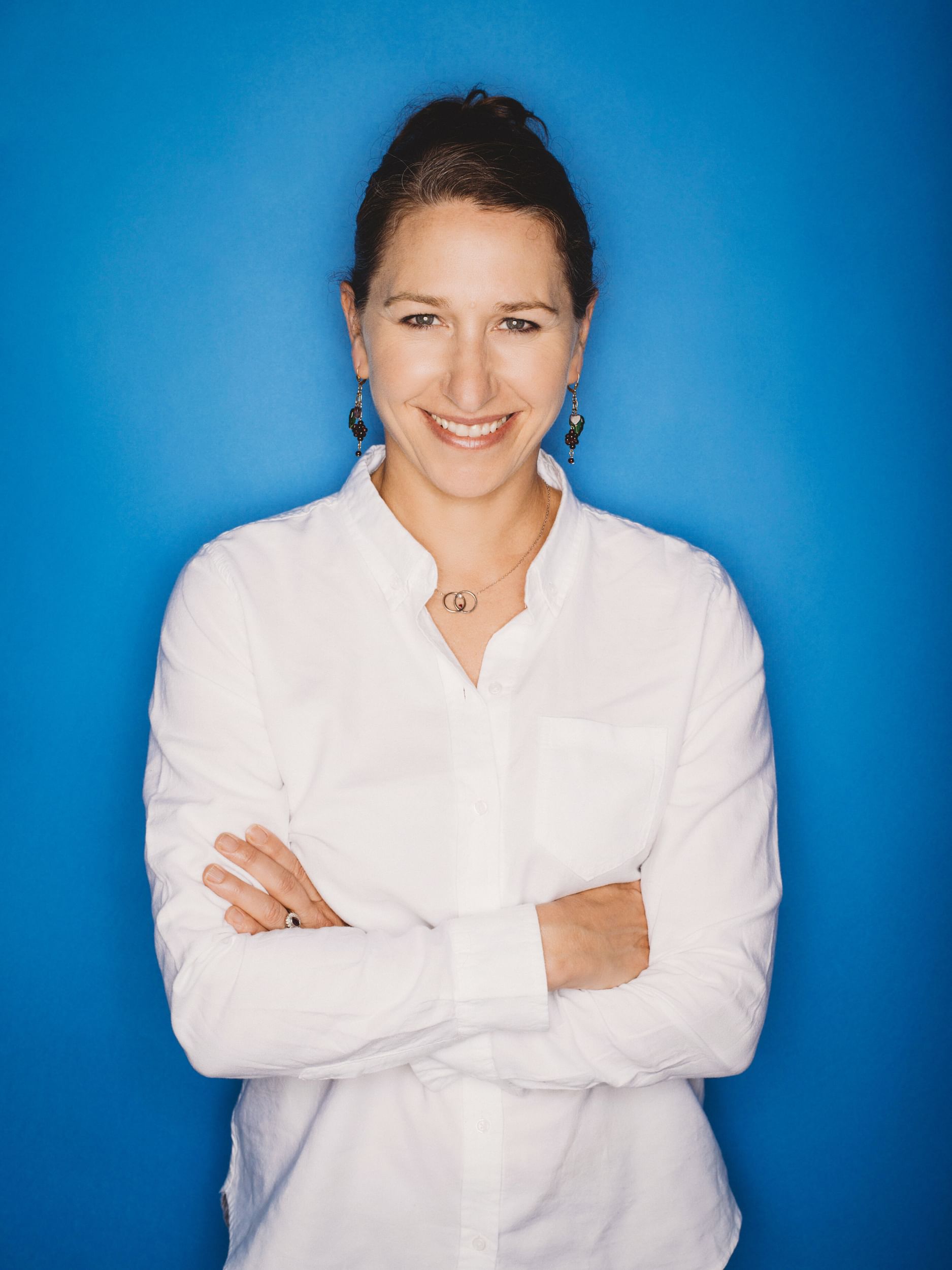 A dancer in an all white top in a portrait shot against a blue backdrop.