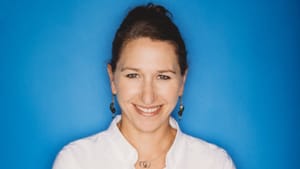 A dancer in an all white top in a portrait shot against a blue backdrop.