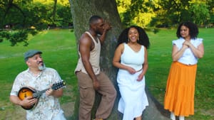 The 4 actors, with different skin tones & genders, pose together in bright, casual summer clothes next to a tree in a park.