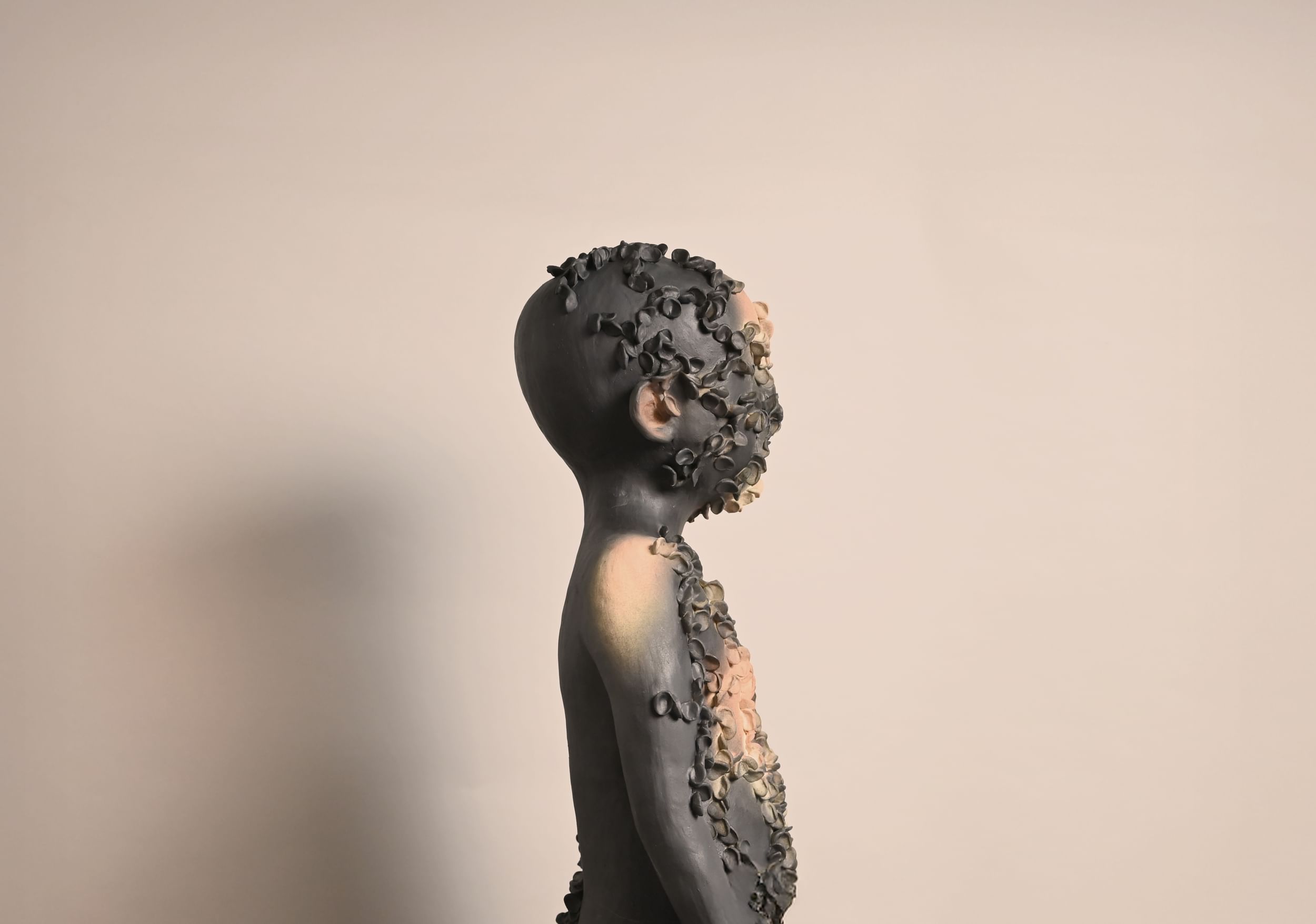 A gray and peach childlike ceramic figure, seen in profile, with bits of pinched clay texturing the front half of its body.