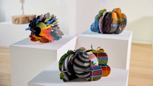 Small, colorful spherical shapes appear to have layers of thin ceramic rounded wings in a collage of bold hues and stripes.