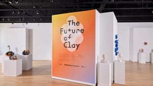Gallery view of show's title wall, with a yellow/orange/purple gradient, and various ceramics on surrounding white pedestals
