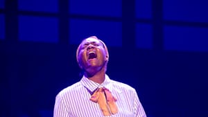 Johnson, a Black woman wearing a long flowered skirt & striped blouse, sings passionately with her hands outspread.