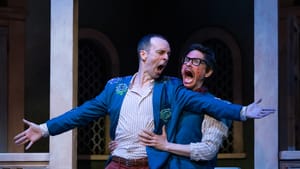 Johnson, in blue jacket with applique roses, spreads his arms while a bespectacled Hernandez grabs him from behind, screaming
