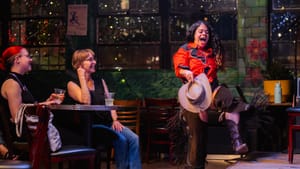 O'Hanlon-Rodriguez in performance, in cowboy attire, steps onto stage in front of the audience, their face wide with exclaim