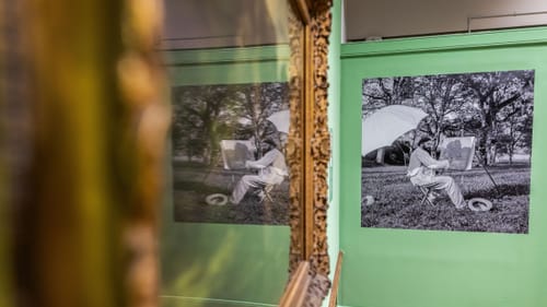 Reproduction of a black & white photo of Courbet working outside, with an easel and white umbrella and jaunty baggy clothes.