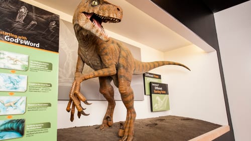 Life-size model of raptor dino with large claws, by signs claiming that God drowned them all in a flood 4,300 years ago.