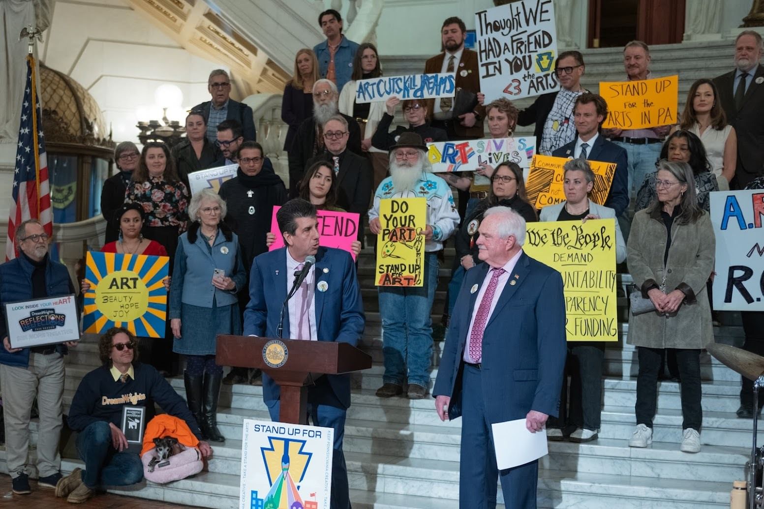 About three dozen people, many with artistic handmade signs with pro-arts slogans, posing on the white steps of the Capitol.