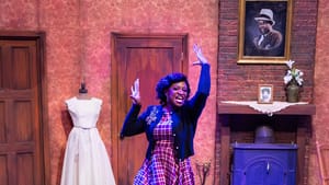 Robinson poses dramatically at center in a plaid dress; Hall & Debose, seen from behind with their hair in buns, look on.