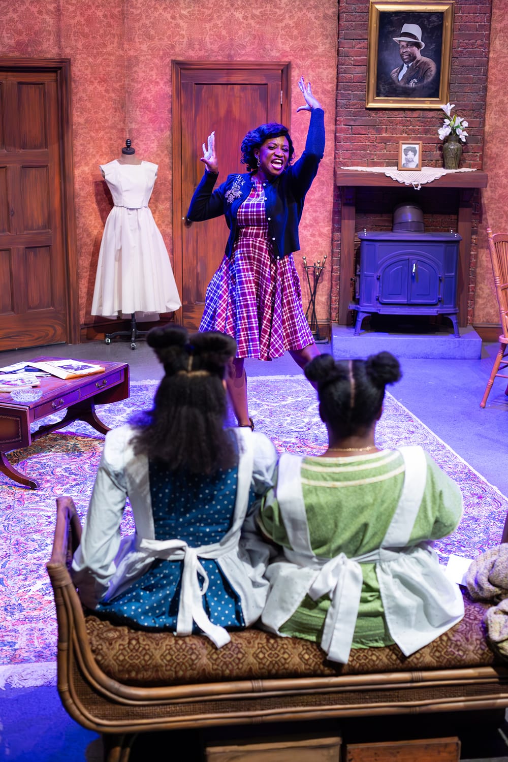 Robinson poses dramatically at center in a plaid dress; Hall & Debose, seen from behind with their hair in buns, look on.