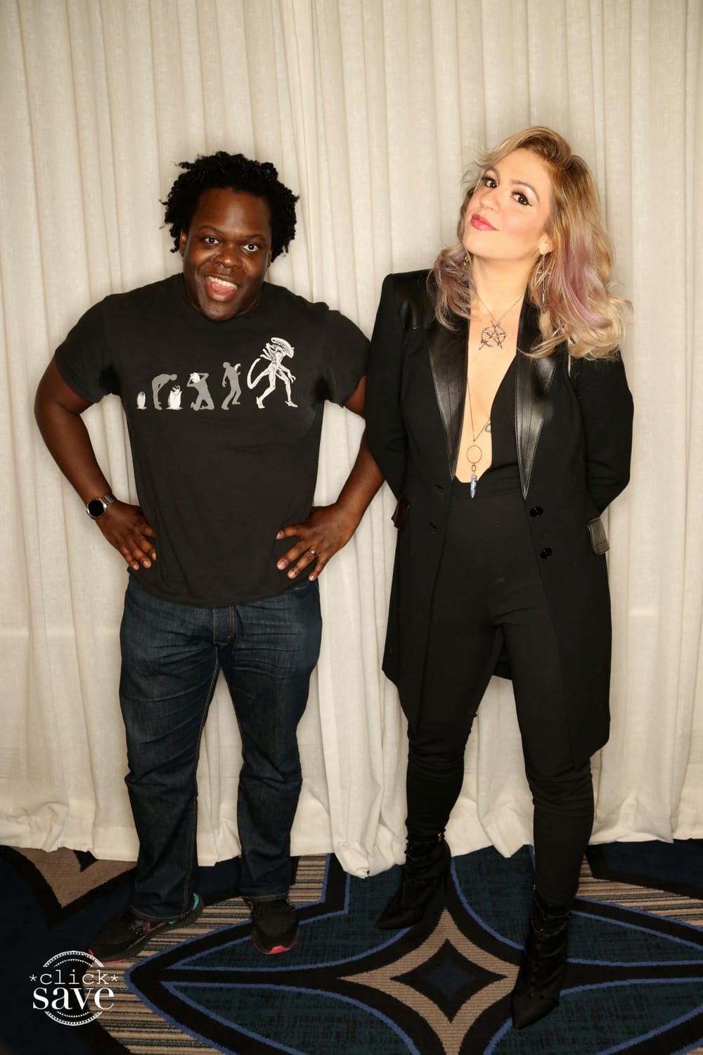 Schmit, Charles pose together. Schmit wears all black with a blazer, Charles in a print T and jeans, against a white curtain