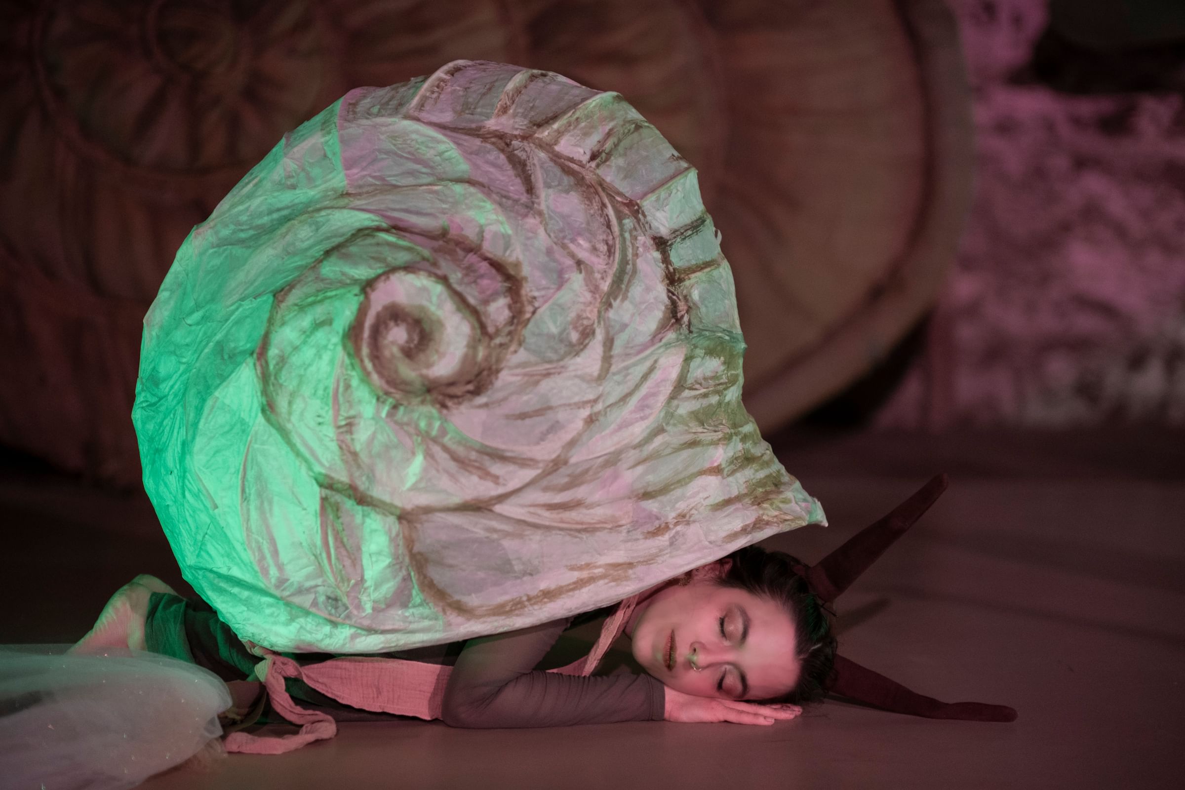 Yatsko poses as if sleeping peacefully, curled up on the floor under a whimsical handcrafted human-sized snail shell.
