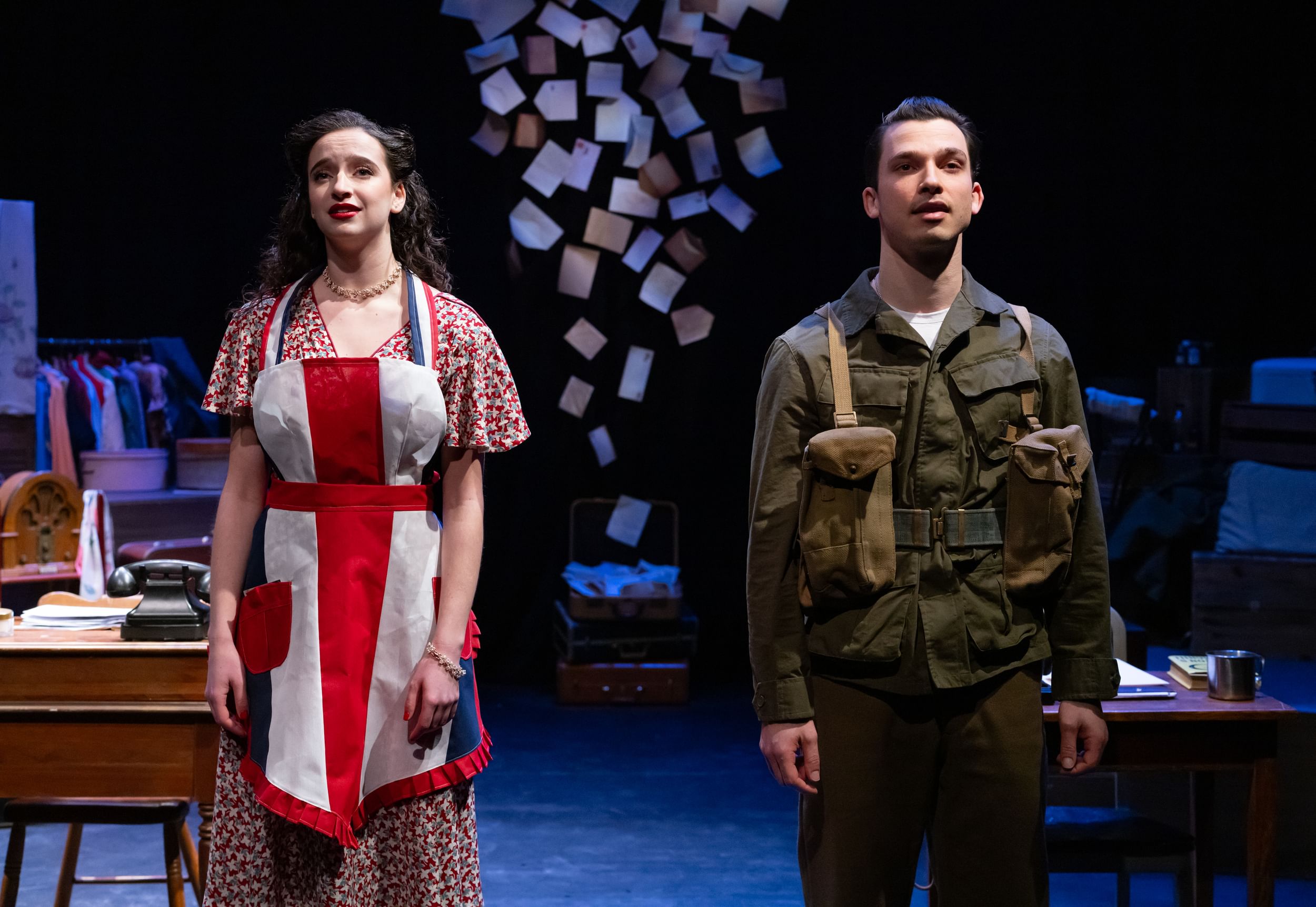 Two people on stage with desks and notes behind them.
