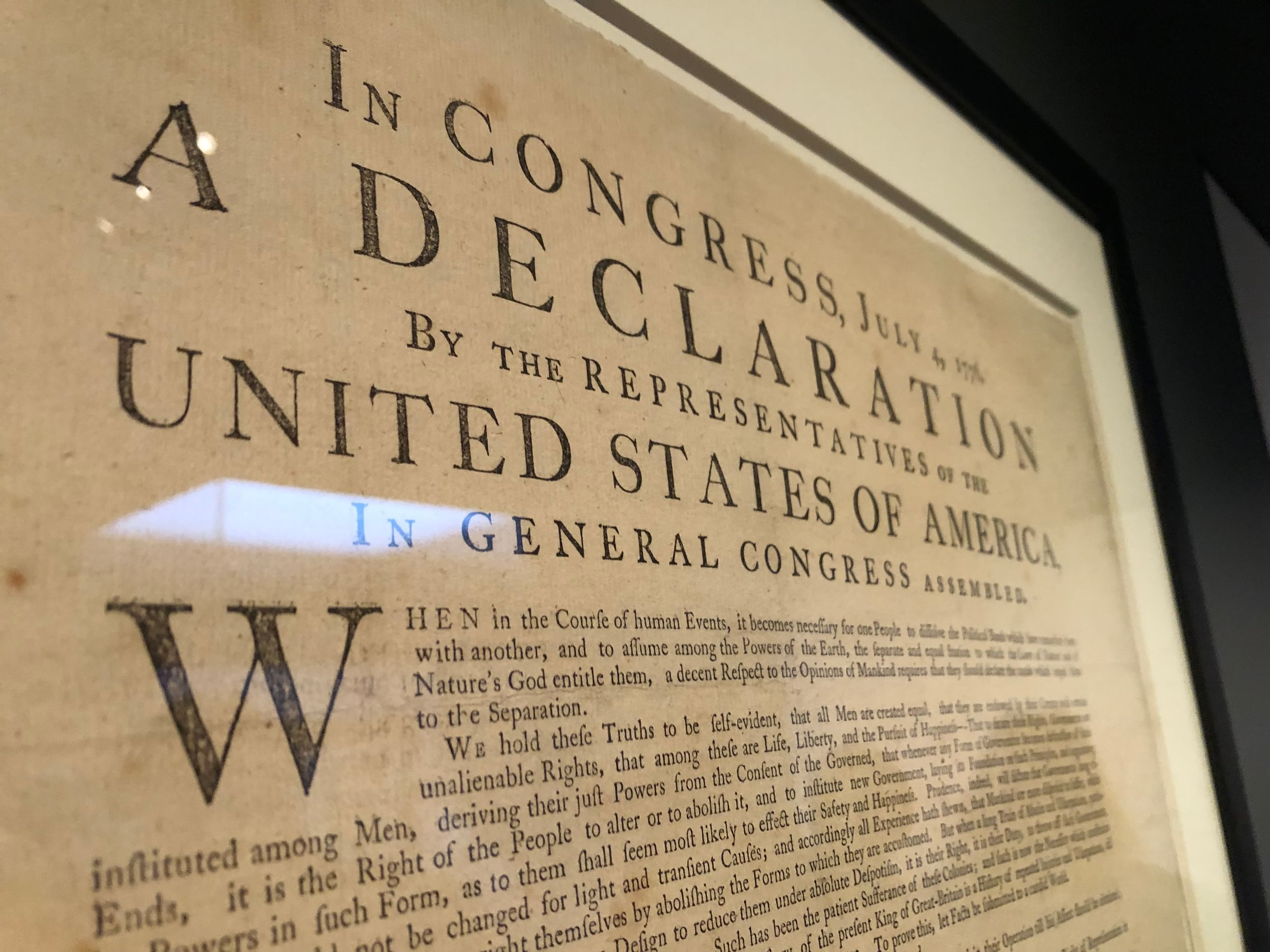 Closeup on the title and opening passages of a framed 1776 printing of the Declaration.