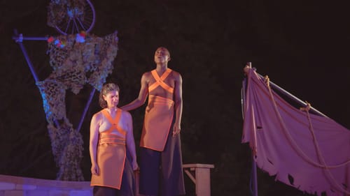 With a dark night behind them, the actors pose together in skin-matching leotards, crossed with orange strips and skirts
