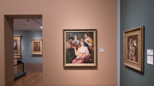 A gallery view with a painting of four classical-looking women in flowing robes. Three are grooming one seated at center