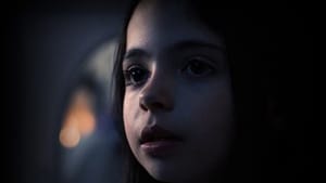Film still features a young girl looking on with onsetting fear with black hair that blends into background