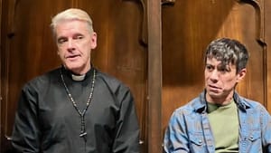 Falango, with short platinum blonde hair, wears a priest's black garb. Del Guzzo, next to him, wears a plaid button down.