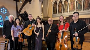 The musicians, all in formal wear, stand in a line on the venue’s chancel. They are smiling and holding their instruments.