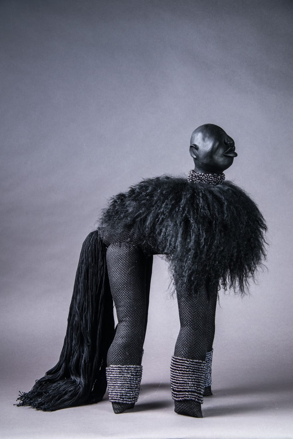 A figure made with black fabrics has four legs, hair, and a tail that gives it a poodle shape, but a human like head