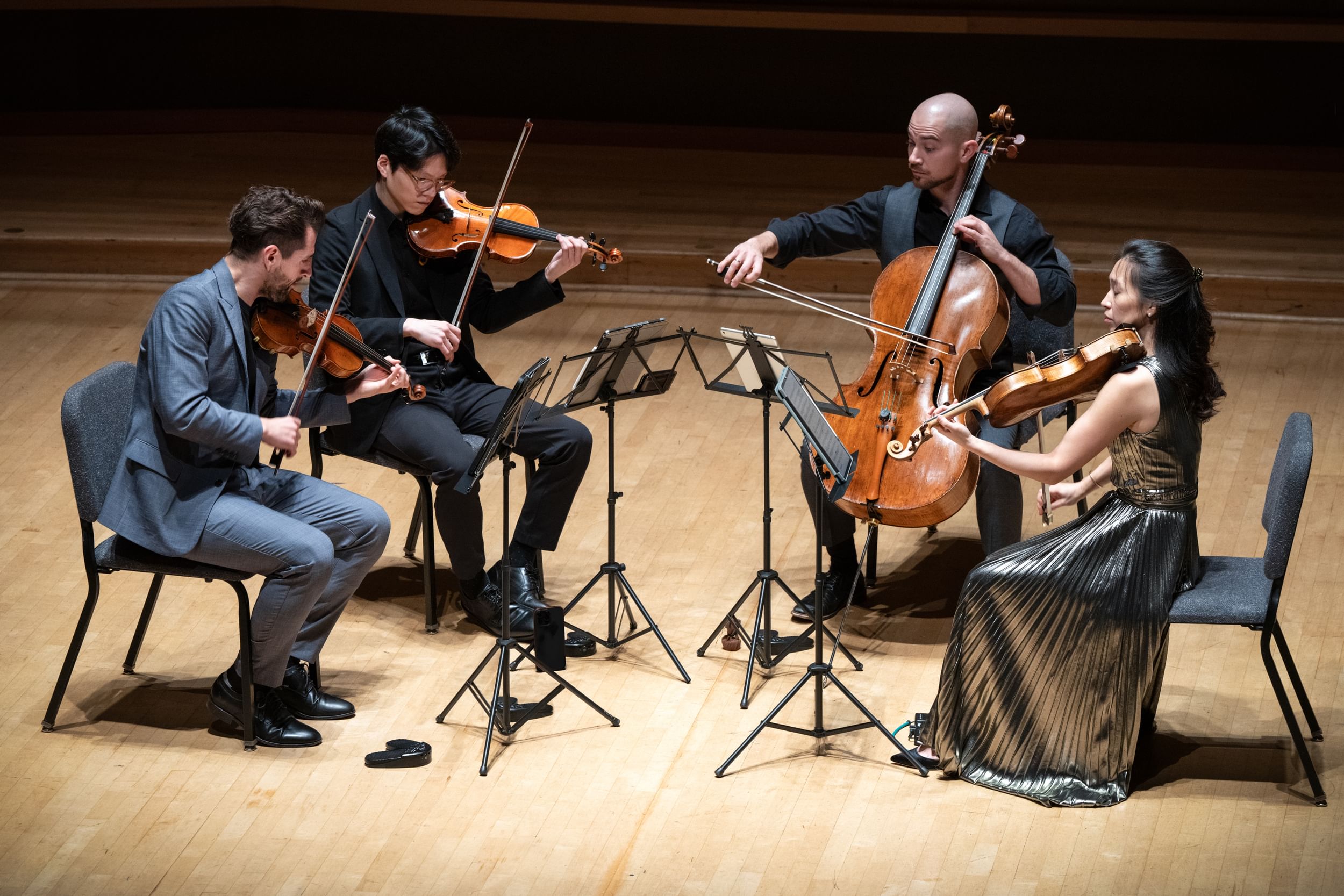 Closeup on the four players in formal wear during the concert, on a light-colored wooden stage.