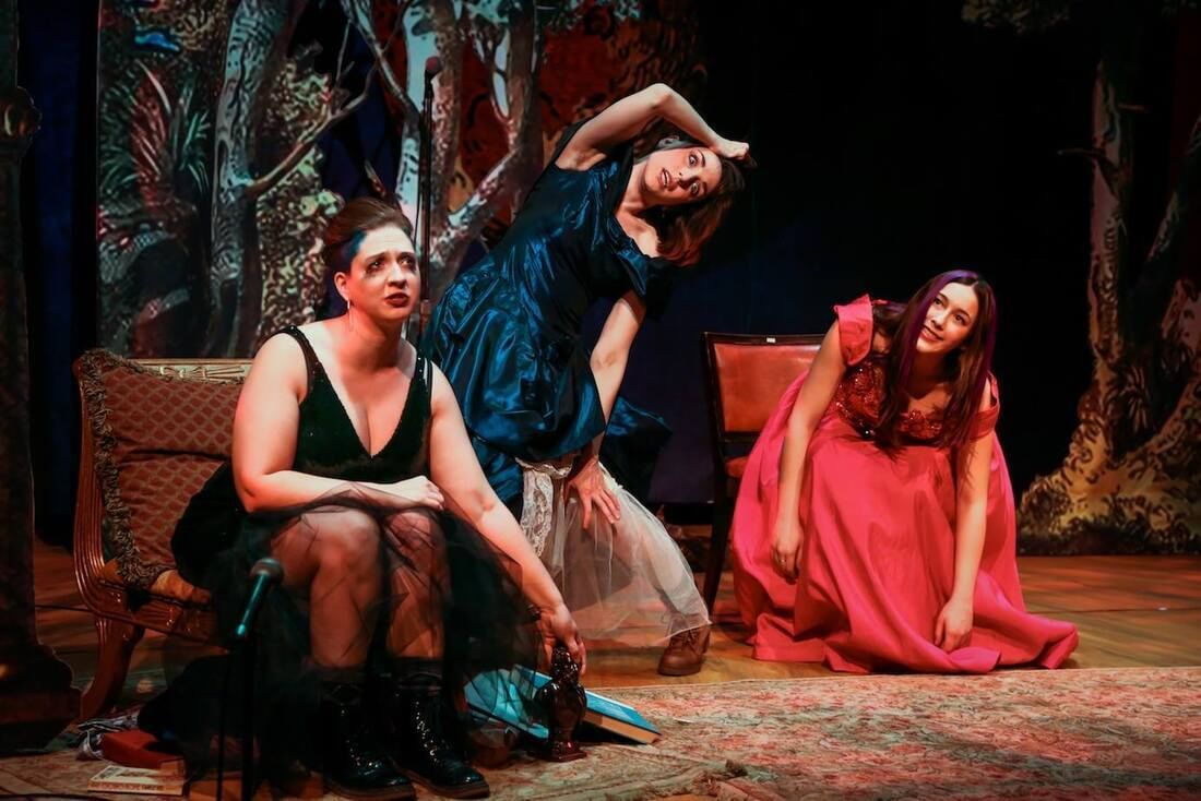 Three performers on stage as vampires in solid colored dresses. Two contort their bodies, another looks out into the audience