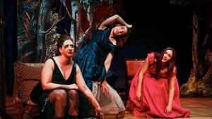 Three performers on stage as vampires in solid colored dresses. Two contort their bodies, another looks out into the audience