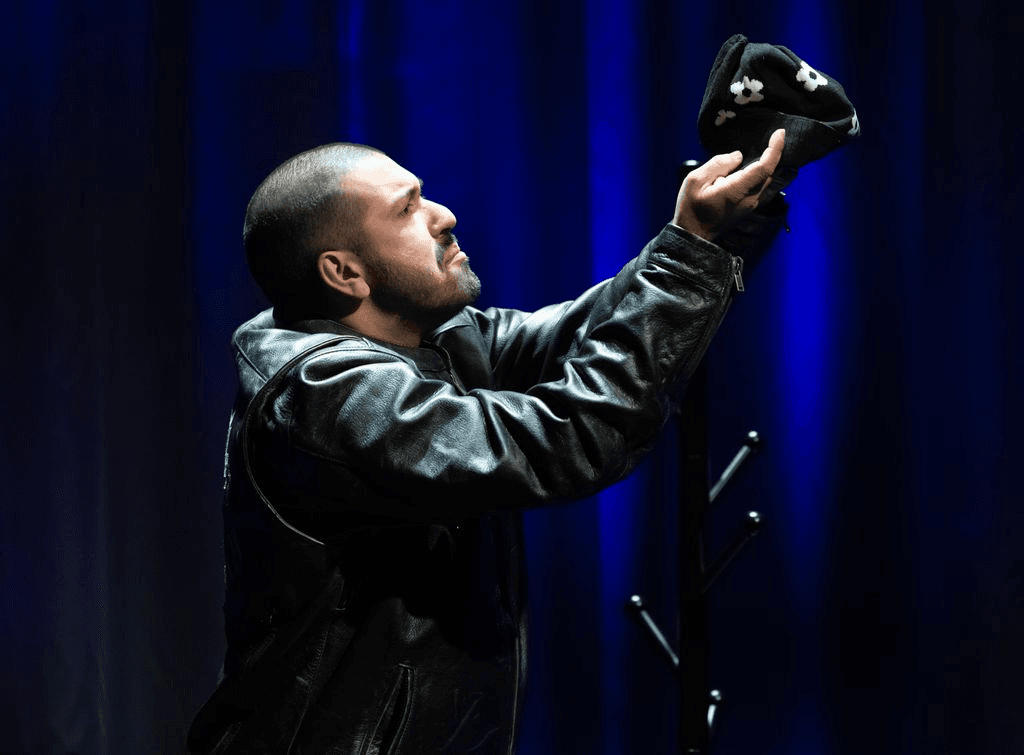 Ahmed, a Southeast Asian person seen in profile wearing a leather jacket, dumps something out of a small black bag.