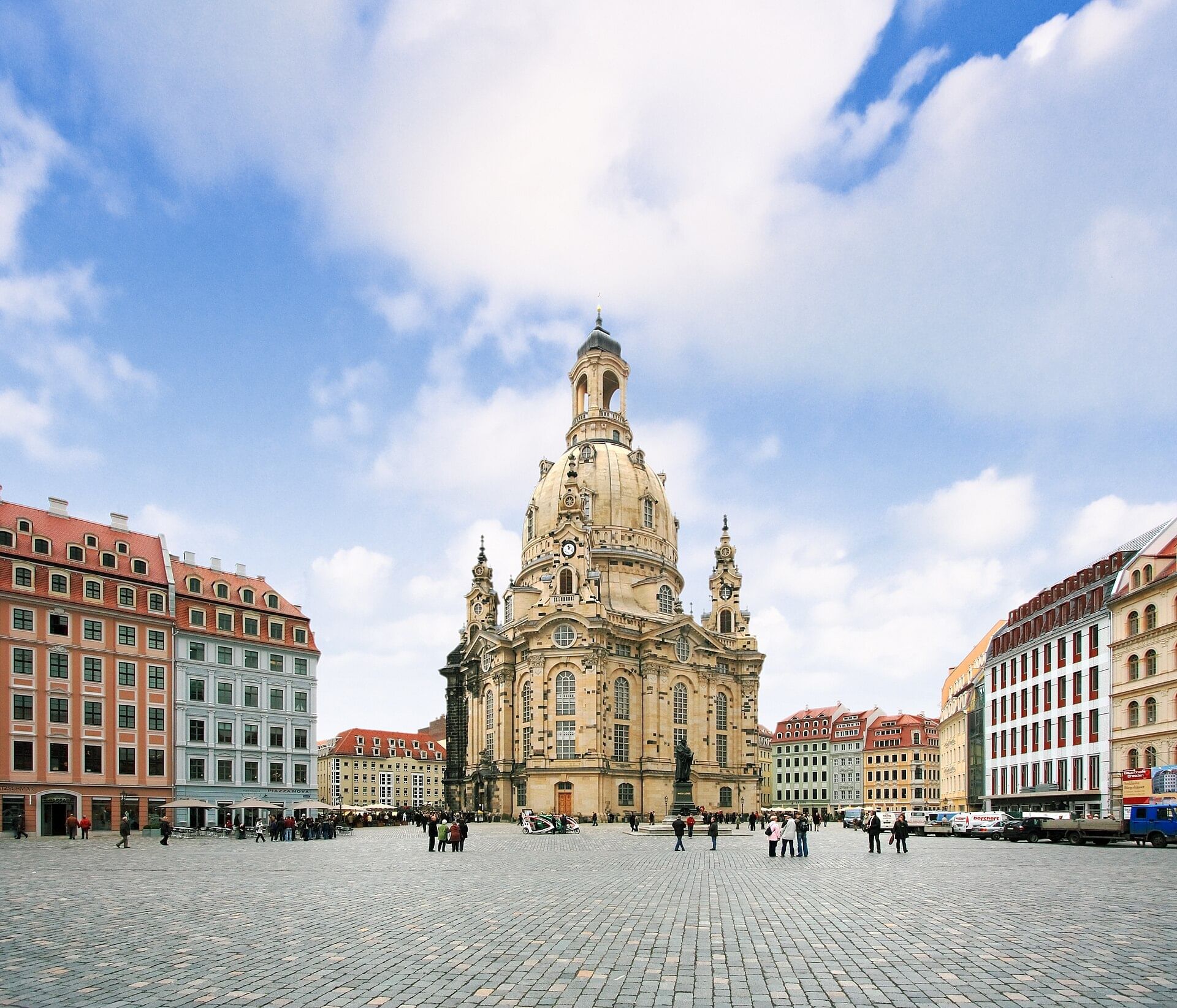 View of historic Dresden square on a sunny day, paved with gray bricks, with an ornate, tan domed building at center.