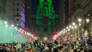 A huge crowd on Philly’s lit-up nighttime Broad Street, under the massive clock tower of City Hall lit up in green.