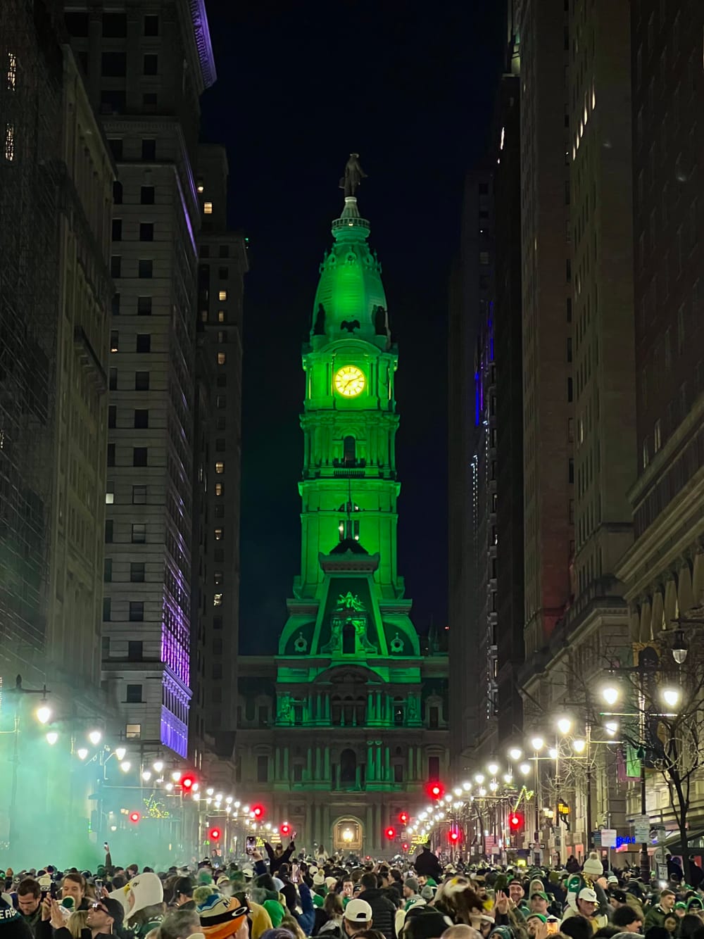A huge crowd on Philly’s lit-up nighttime Broad Street, under the massive clock tower of City Hall lit up in green.