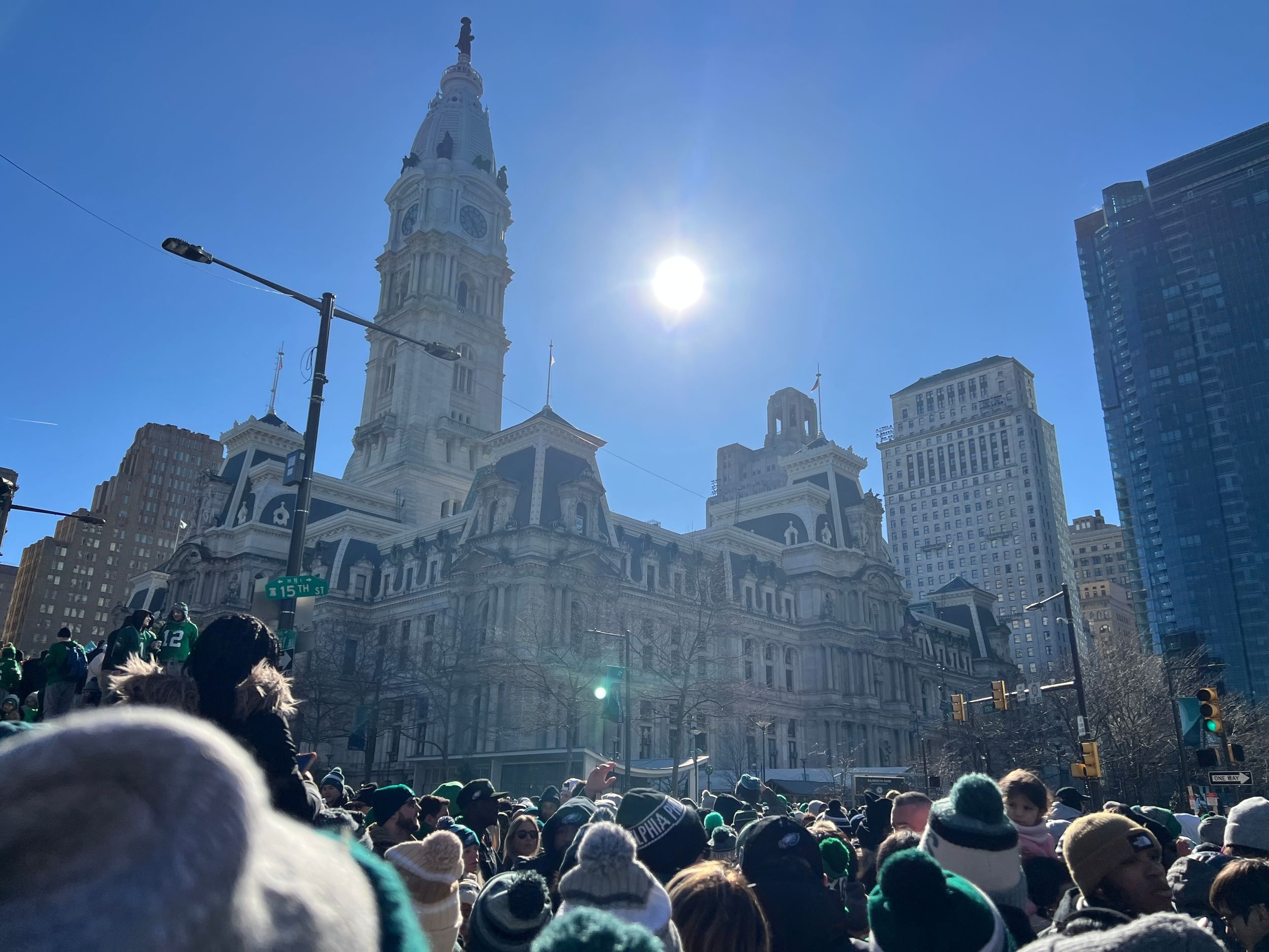 A huge crowd of Eagles fans in green surrounds Philly’s City Hall, the sun shining above in a bright blue winter sky.