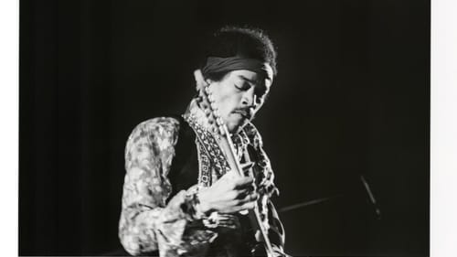 Black & white photo of Hendrix onstage, shown from the waist up intent on playing his guitar.