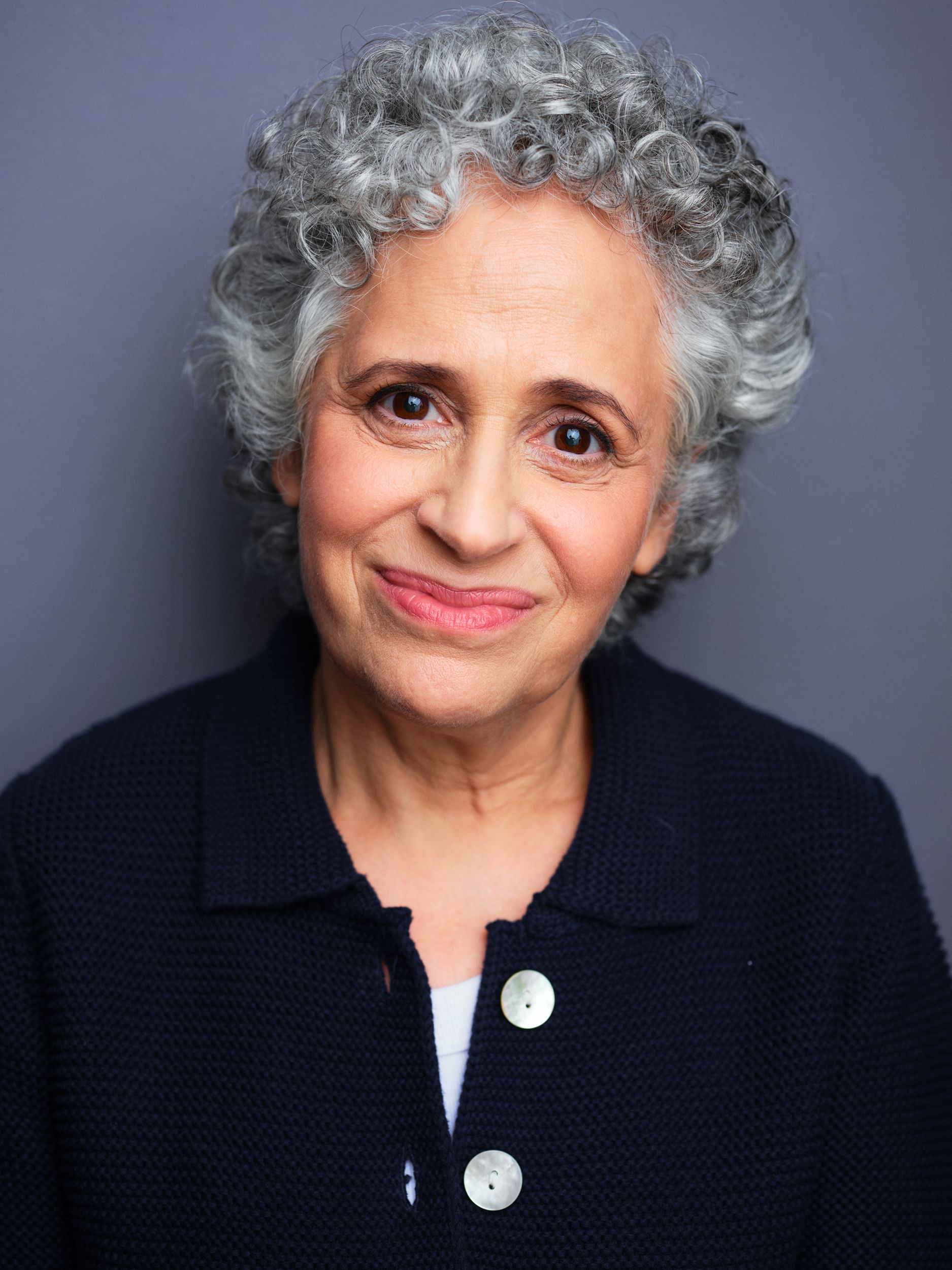 Headshot of Boscov, a woman with salt and pepper hair, wears a dark blue sweater with large white buttons