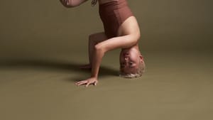 Godfrey, a nonbinary dancer of Korean heritage, poses in a headstand, legs bent in a graceful S shape.