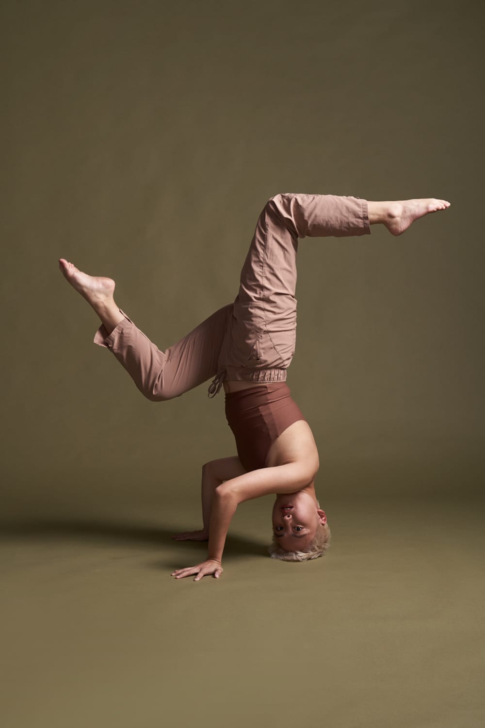 Godfrey, a nonbinary dancer of Korean heritage, poses in a headstand, legs bent in a graceful S shape.