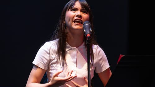 Thammavong, a young Asian person in a short-sleeve white button-down, speaks passionately into a mic.