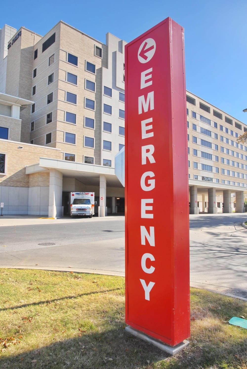 An exterior photo of a hospital with a large vertical sign that says “emergency” in red letters.