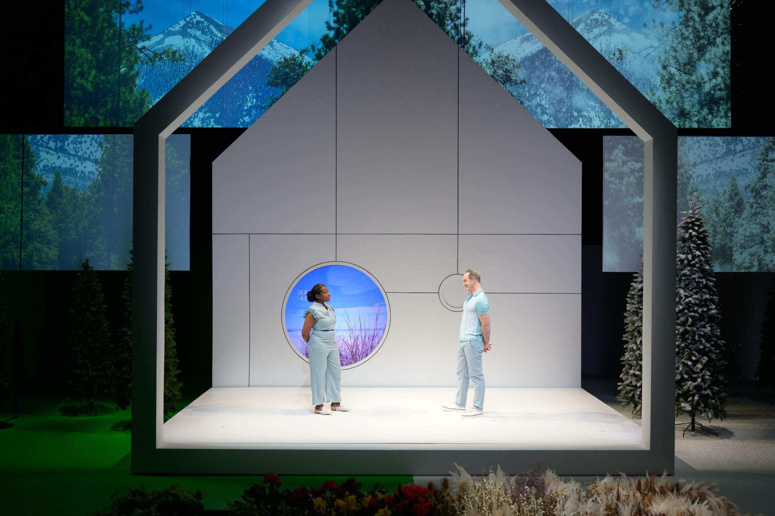 Kidwell & Rishard, in light blue outfits, face each other in a white house-shaped structure with round blue/purple-lit window