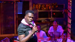 In the foreground, Thomas sings passionately into a mic, with the others behind him on a porch awash in purple light.