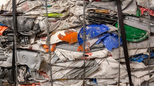 Close-up on a compressed block of plastic trash, with scraps of white, orange, gray, blue, red, green, and yellow.