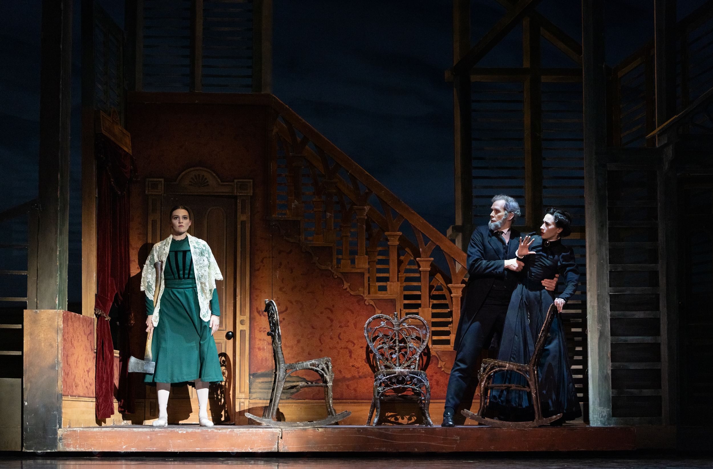 In a set like a 19th century home, Dolan, in green, holds an axe, facing forward. At right, her parents, in black, cower