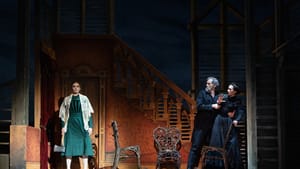 In a set like a 19th century home, Dolan, in green, holds an axe, facing forward. At right, her parents, in black, cower