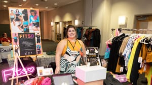 FITSO’s vendor table, clothes by the table with a cloth with the co. logo. A sign on an easel behind the person at the table