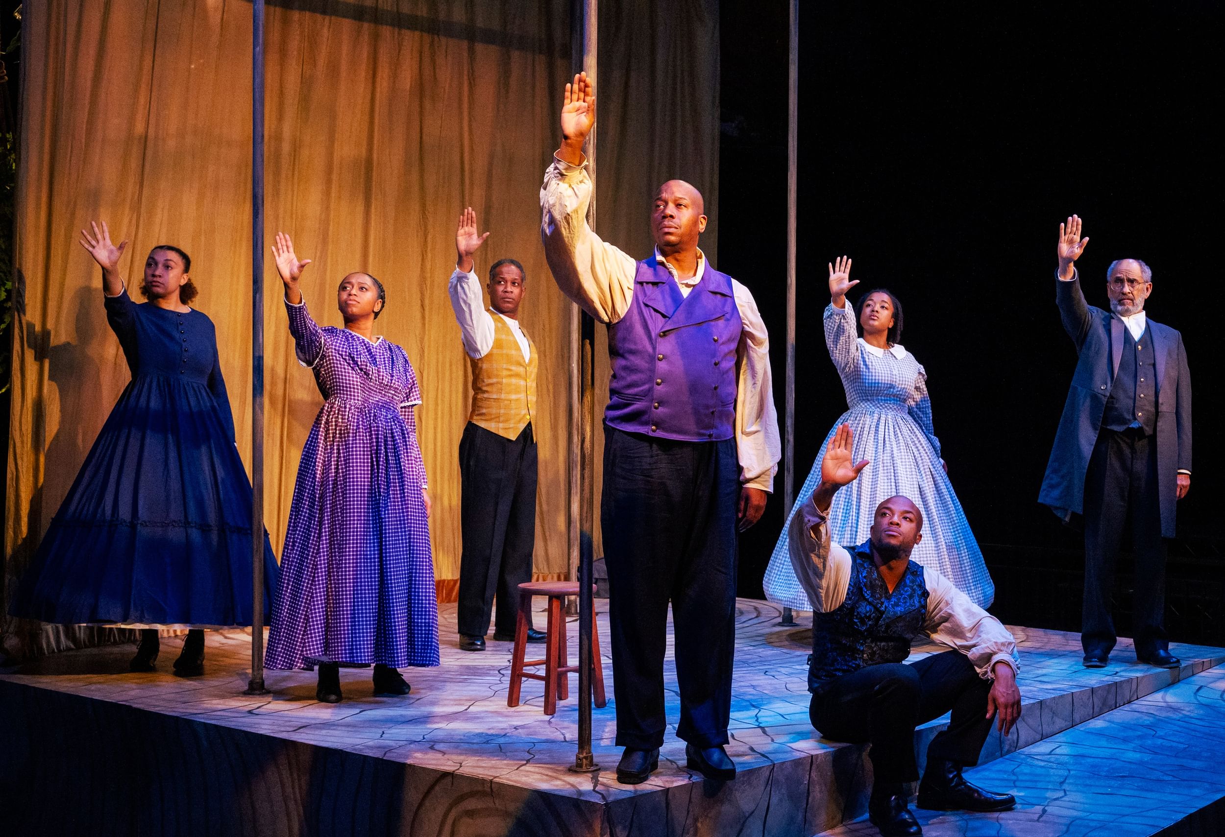 In Civil War era costumes, the cast poses onstage looking gravely to the right, each raising their right hand, palm outward.